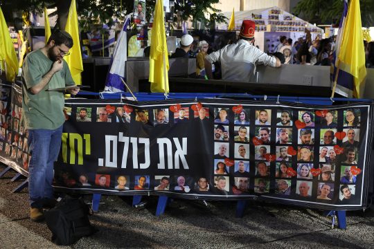 Ein Mann steht auf einem Platz in Tel Aviv neben einem Transparent mit Bildern israelischer Geiseln