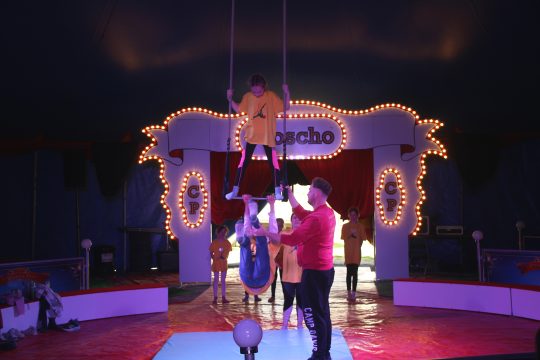 Kinder studieren eine Trapeznummer ein, daneben steht ein Trainer