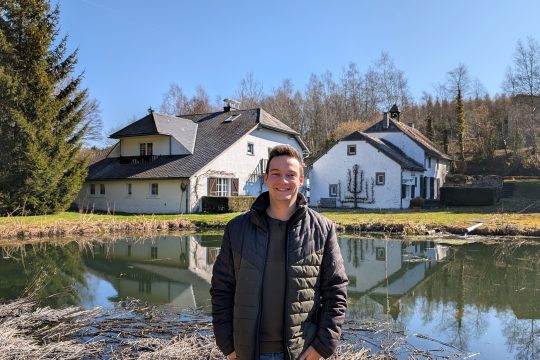 Gillian Fuhrmann steht vor einem kleinen Teich, dahinter steht dann die Alte Mühle in Weywertz