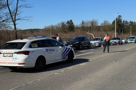Ein belgischer Polizeiwagen und ein belgischer Polizist sind zu sehen, am Fahrbahnrand stehen Autos
