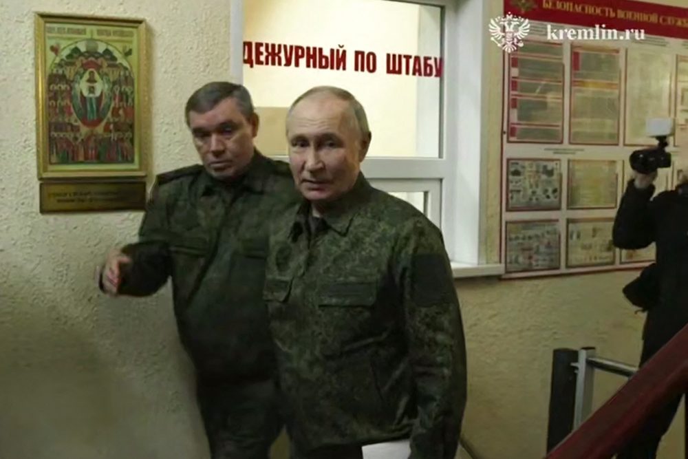 Wladimir Putin im Armee-Tarnanzug im Flur eines Gebäudes, neben ihm geht ein Angehöriger des Militärs