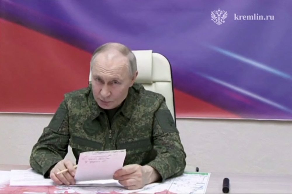 Russlands Präsident Wladimir Putin sitzt im militärischen Tarnanzug auf einem Stuhl an einem Tisch mit einem Papier in der Hand