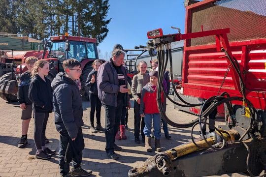 Kinder stehen vor einem Traktor und bekommen etwas erklärt