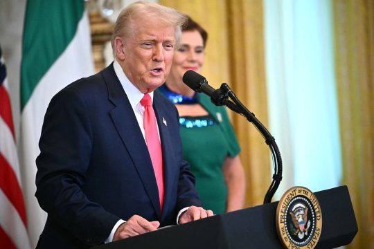 US-Präsident Donald Trump steht vor dem Rednerpult und spricht, im Hintergrund ist eine Frau zu sehen