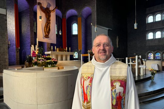 Claude Theiss steht im Pfarrgewand in der Kirche, vor dem Altarbereich