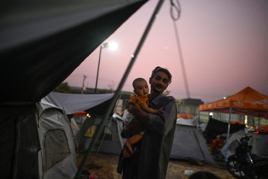 Mann mit Baby vor Zelten in einem improvisierten Lager in der Nähe von Mandalay