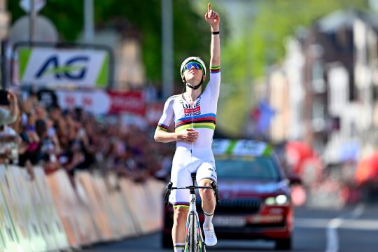 Tadej Pogacar streckt jubelnd einen Arm in die Höhe und hält den Zeigefinger hoch, als er über die Ziellinie fährt