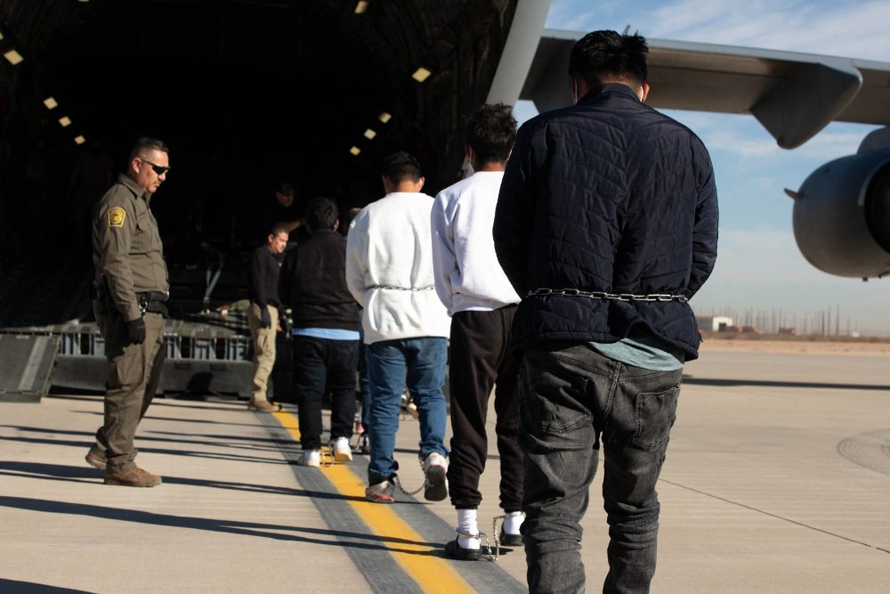 Migranten gehen in Richtung eines bereitstehenden Flugzeugs für ihre Abschiebung, links im Bild ein Beamter der Abschiebepolizei