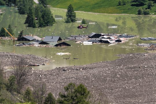 Ein Hubschrauber fliegt über Trümmern und zerstörten Häusern des überschwemmten Dorfes Blatten