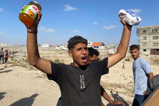 Ein junger Mann hebt beide Hände in die Höhe, in der einen hält er ein Marmeladenglas, in der anderen eine Packung Mehl