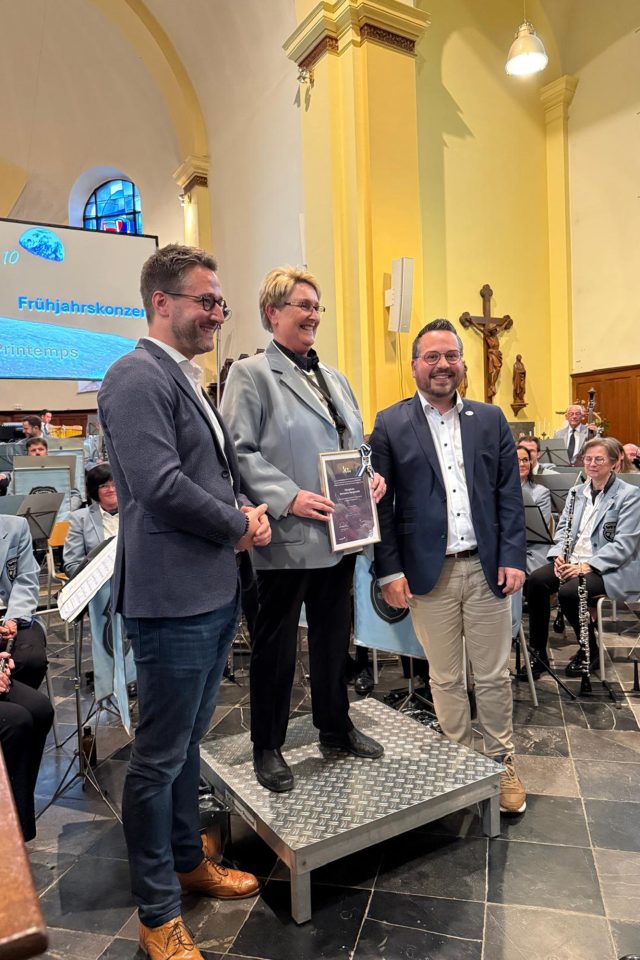 Bürgermeister Daniel Hilligsmann und der Erste Schöffe Björn Klinkenberg überreichen die Auszeichnung an die Dirigentin der Harmonie Hergenrath