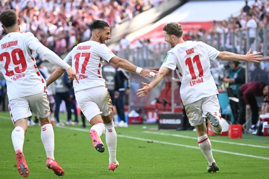 Drei Spieler des 1. FC Köln sind von hinten zu sehen, wie sie jubelnd über das Spielfeld laufen