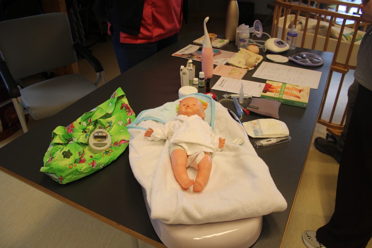 Eine Babypuppe, Utensilien zur Babypflege und Informationsdokumente liegen auf einem Tisch