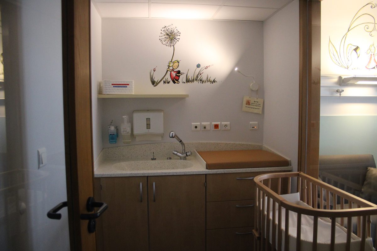 Babybettchen neben einem Zimmer der Wochenstation, im Hintergrund ein Waschbecken und eine Wickelauflage