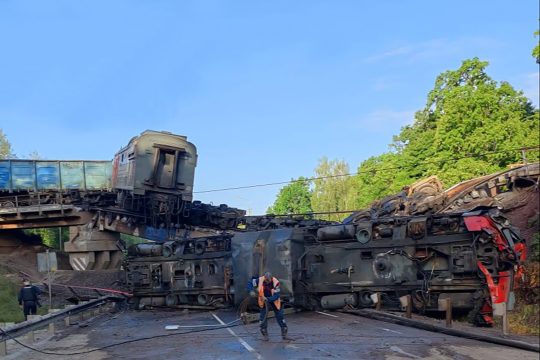 Auf der eingestürzten Brücke hängt ein Waggon halb in der Luft, unten auf dem Boden liegt die Lokomotive auf der Seite und ist völlig zerstört, ein Arbeiter ist im Vordergrund zu sehen