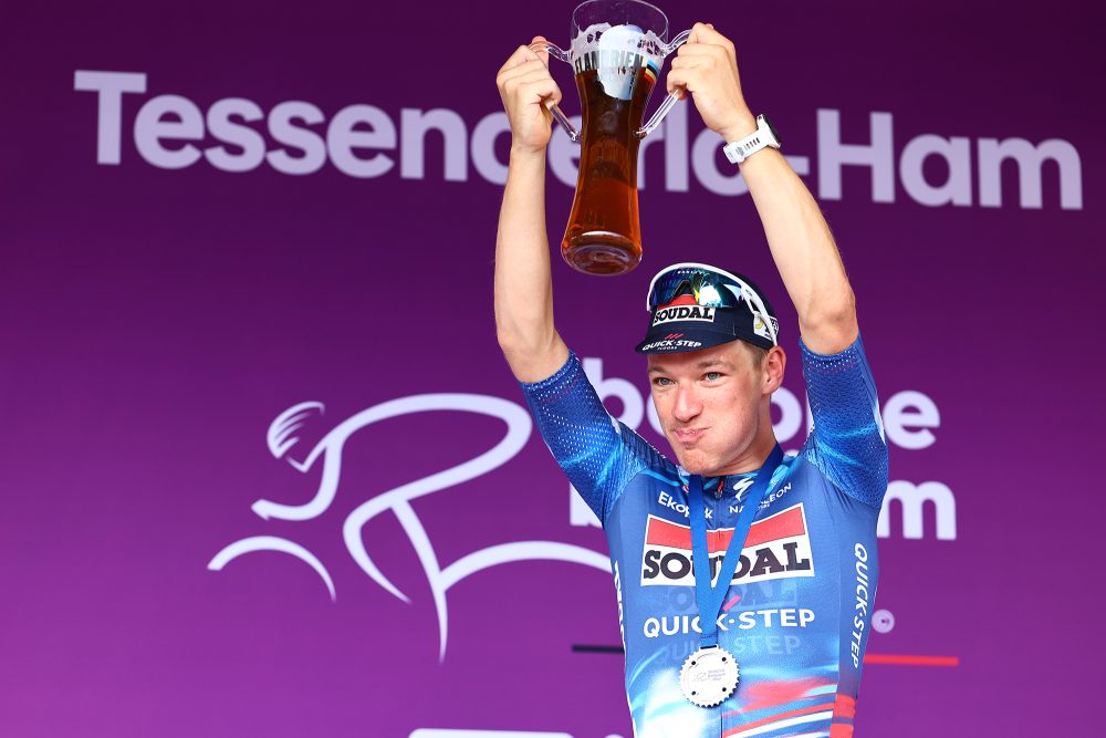 Der britische Radprofi Ethan Hayter mit Medaille um den Hals hält bei der Siegerehrung mit beiden Händen ein großes Bierglas hoch