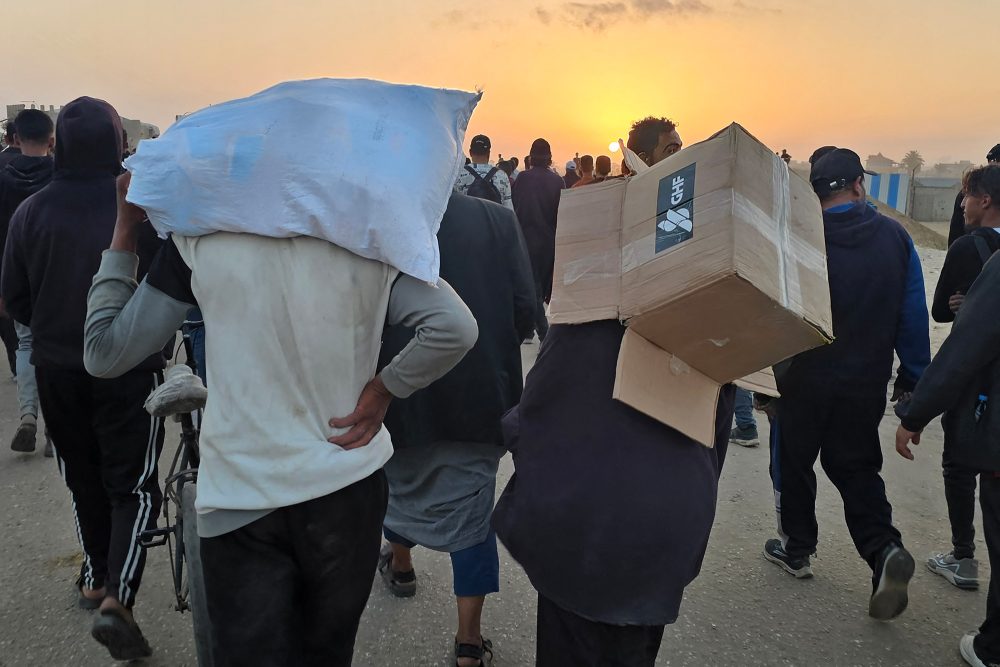 Menschen von hinten, die am Gehen sind, einer trägt einen Sack auf den Schultern, ein anderer hält einen leeren Karton
