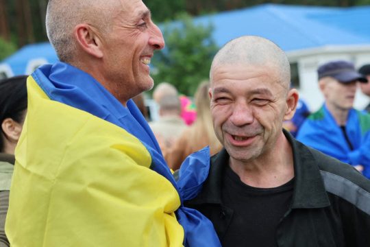 Ukrainische Kriegsgefangene lächeln nach ihrer Freilassung, einer hat sich mit der ukrainischen Nationalflagge umhüllt
