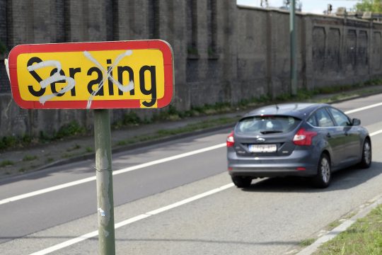 Ortsschild von Seraing an einer Straße, auf gerade ein Auto fährt