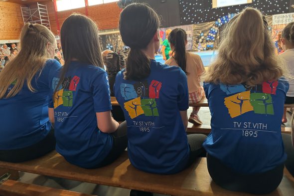 Mehrere Mädchen von hinten, die in Richtung der Hallenmitte schauen - sie tragen T-Shirts des Turnverein St. Vith