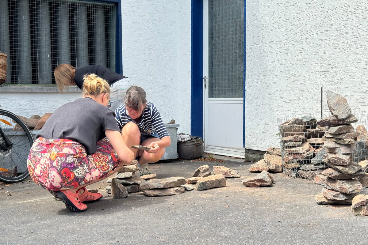 Teilnehmerinnen knien über dem Boden, auf dem Steine liegen, die zum Basteln verwendet werden