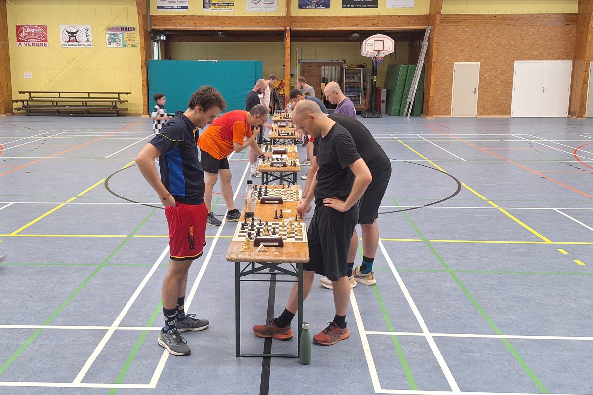 In der Sporthalle sind mehrere Tische mit Schachbrettern aufgebaut, um sie herum stehen die Spieler