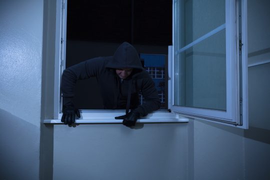 Einbrecher steigt durch ein Fenster in eine Wohnung