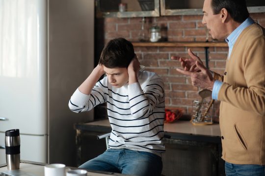 Vater diskutiert mit Sohn, der sich die Ohren zuhält