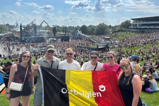 Ostbelgische Fans bei Tomorrowland 2025 halten gemeinsam eine belgische Nationalflagge mit der Aufschrift "Ostbelgien"