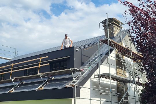 Dachdecker Andre Colgen steht auf dem Dach eines Hauses und arbeitet
