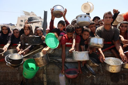 Menschen stehen mit Kochtöpfen und Schüsseln an einer Essenausgabe in Gaza-Stadt
