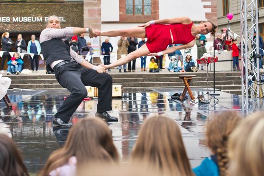 Ein Artist hält eine Artistin an ihren Füßen fest und wirbelt sie um sich herum