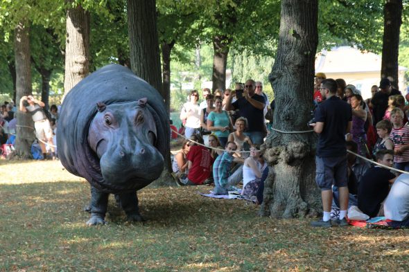 Große Steinfigur eines Hippopotamus in einem Park, daneben stehen Kinder