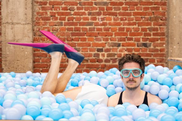 Künstler liegt mit Schwimmbrille und Schwimmflossen in einem Bällebad