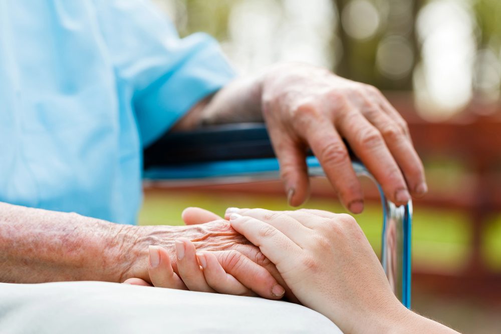 Senior im Rollstuhl mit der Hand einer Pflegekraft