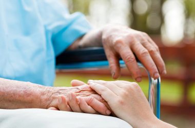 Senior im Rollstuhl mit der Hand einer Pflegekraft