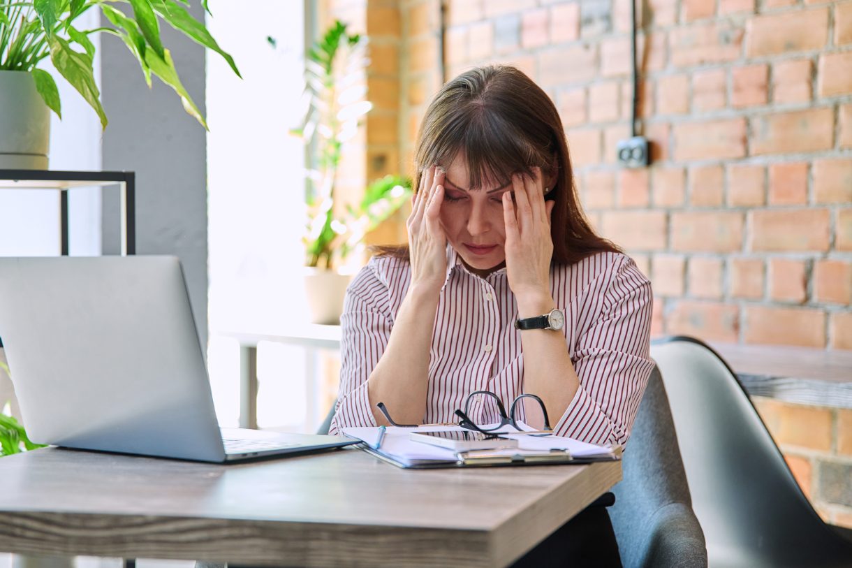 eine Frau hält die Hände an ihre Schläfen - sie sind an einem Bürotisch