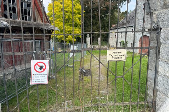 Verschlossenes Zufahrtstor zum Burggelände, Bauzäune vor einem verfallenden Gebäude