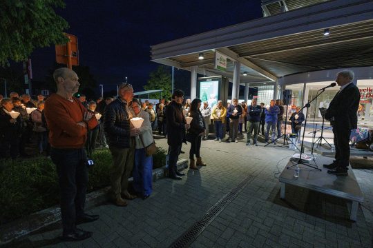 Menschen mit Kerzen versammeln sich auf dem Supermarkt-Parkplatz, ein Mann hält eine Rede