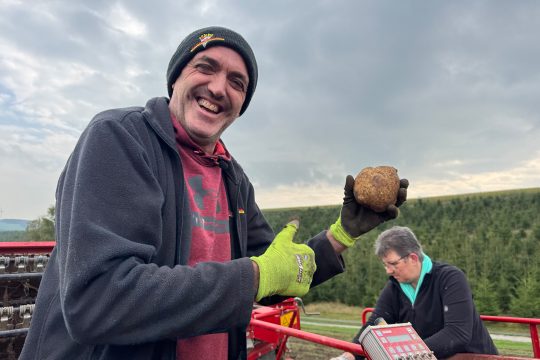 Kartoffelbauer Robert Wangen hält eine Kartoffel in der Hand und lacht
