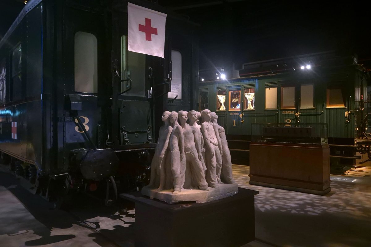 Alte Eisenbahnwaggons, davor eine Skulptur einer Gruppe von Menschen