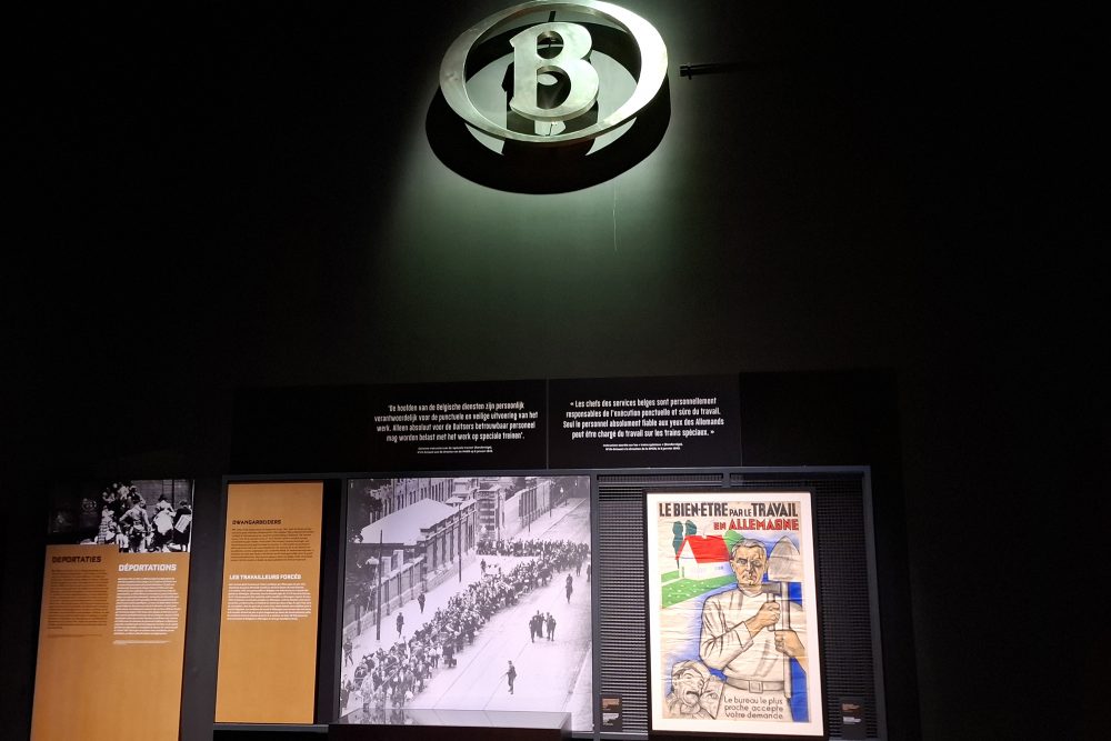 Das Logo der belgischen Staatsbahn, darunter eine Tafel sowie ein Foto aus der Zeit des Zweiten Weltkriegs