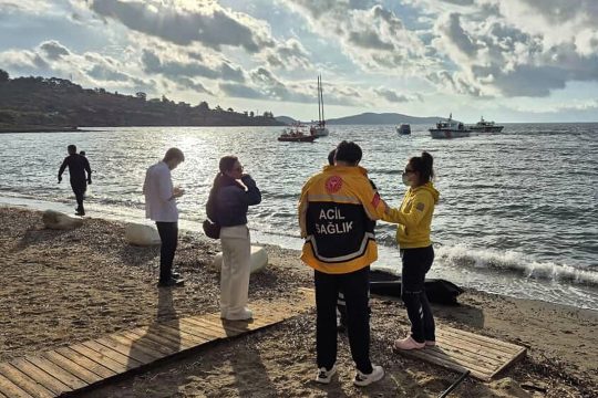 griechische Rettungskräfte neben dem Körper eines ertrunkenen Flüchtlings, im Hintergrund sucht ein Boot nach weiteren Opfern