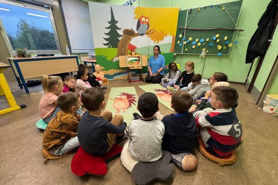 Kinder sitzen für eine Erste-Hilfe-Übung auf dem Boden