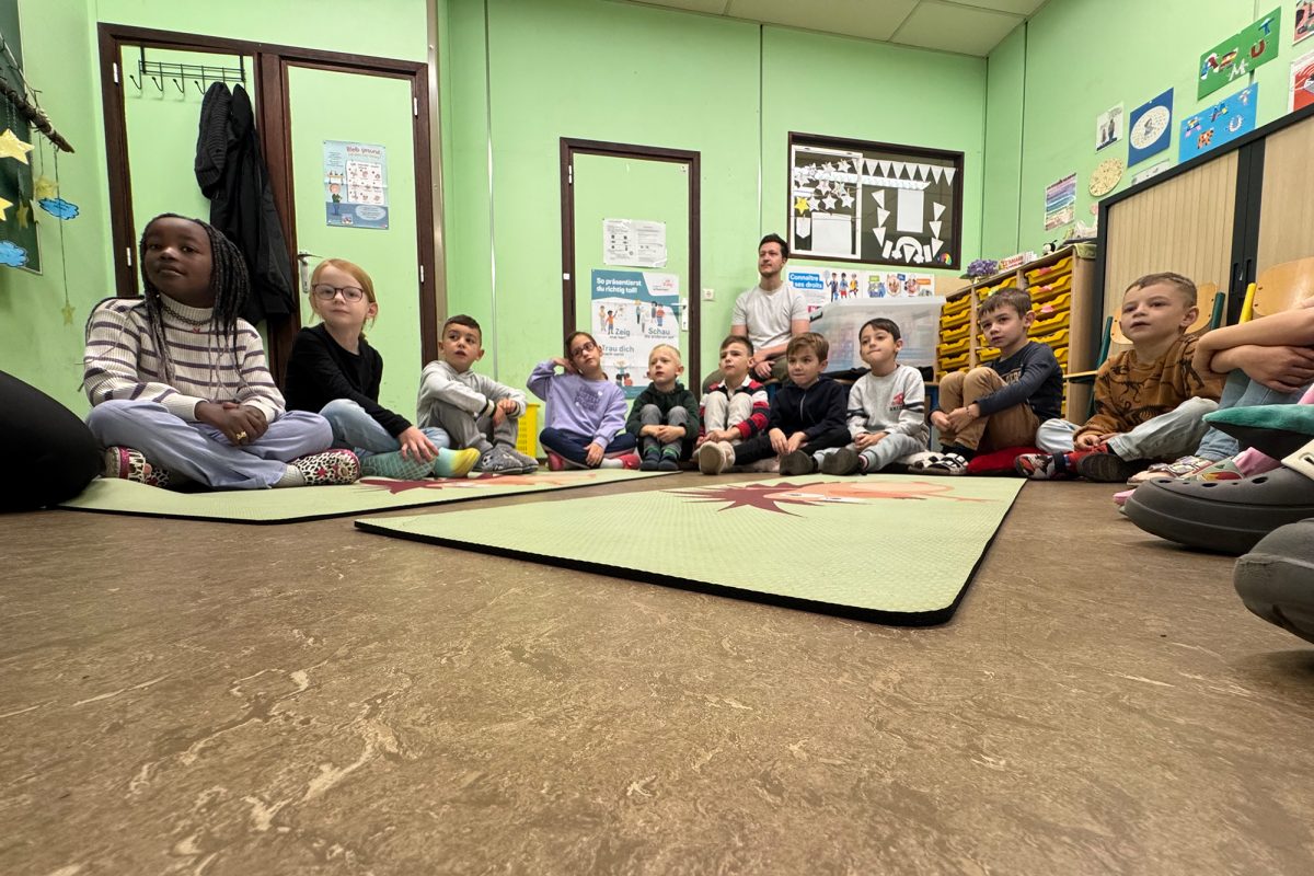 Kinder sitzen für eine Erste-Hilfe-Übung auf dem Boden