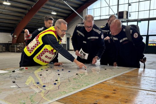 Feuerwehrleute bei einer Einsatzbesprechung, vor ihnen liegt eine große Landkarte ausgebreitet auf einem Tisch