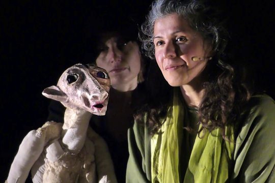 Puppenspielerin mit Puppe, im Hintergrund eine weitere Frau