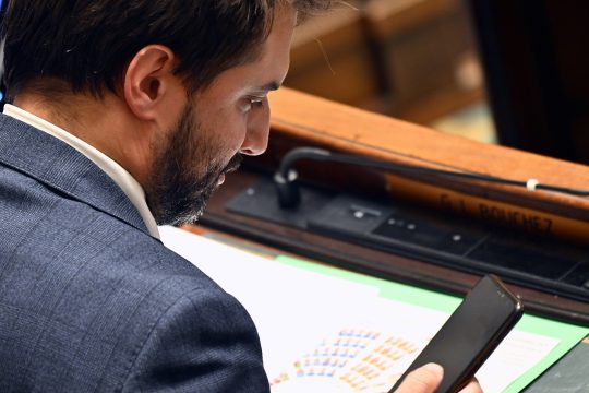 Georges-Louis Bouchez sitzt in der Kammer und schaut auf sein Handy