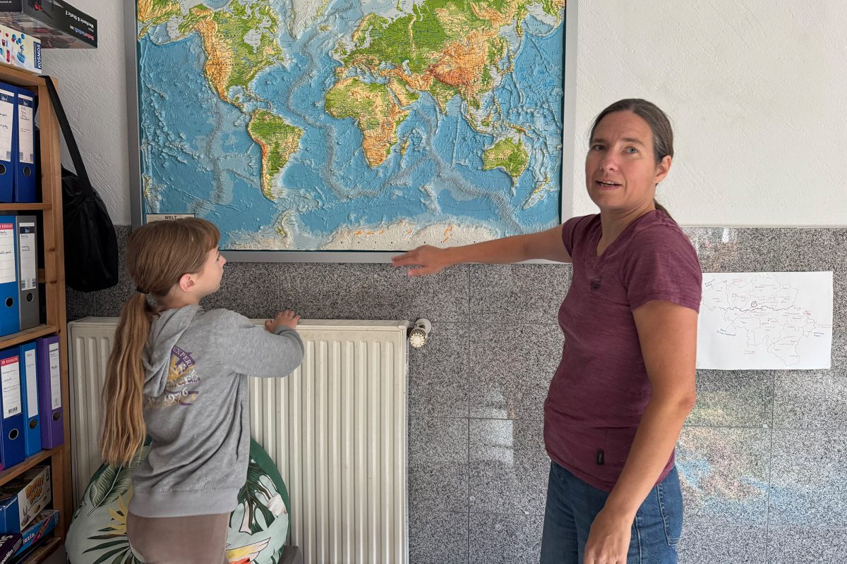 Mutter Michaela Tjarks zeigt auf eine Weltkarte an der Wand, Tochter Fynja steht neben ihr