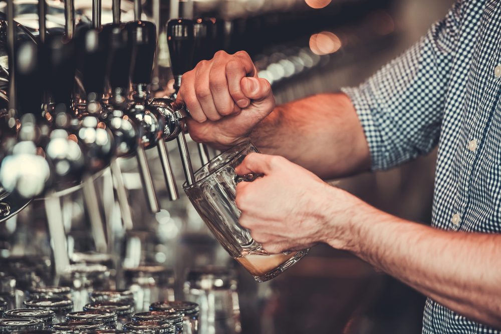 Hände eines Mannes in Nahaufnahme, der gerade ein Bier am Tresen einer Kneipe zapft